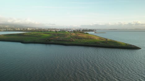 vista aérea del parque césar chávez, una península que se extiende en la bahía de san francisco, con campos de hierba, aguas tranquilas y el paisaje urbano de berkeley en la distancia bajo un cielo nublado