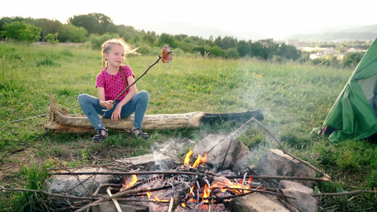 la niña inesperadamente dejó caer el palo de salchicha en la fogata y se rió graciosamente de ello sentada en el campamento de tiendas de campaña. actividades de picnic al aire libre de la familia concepto de imágenes 4k.