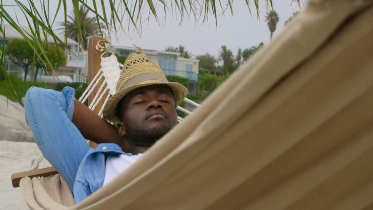 Front view of African american man sleeping in a hammock on the beach 4k