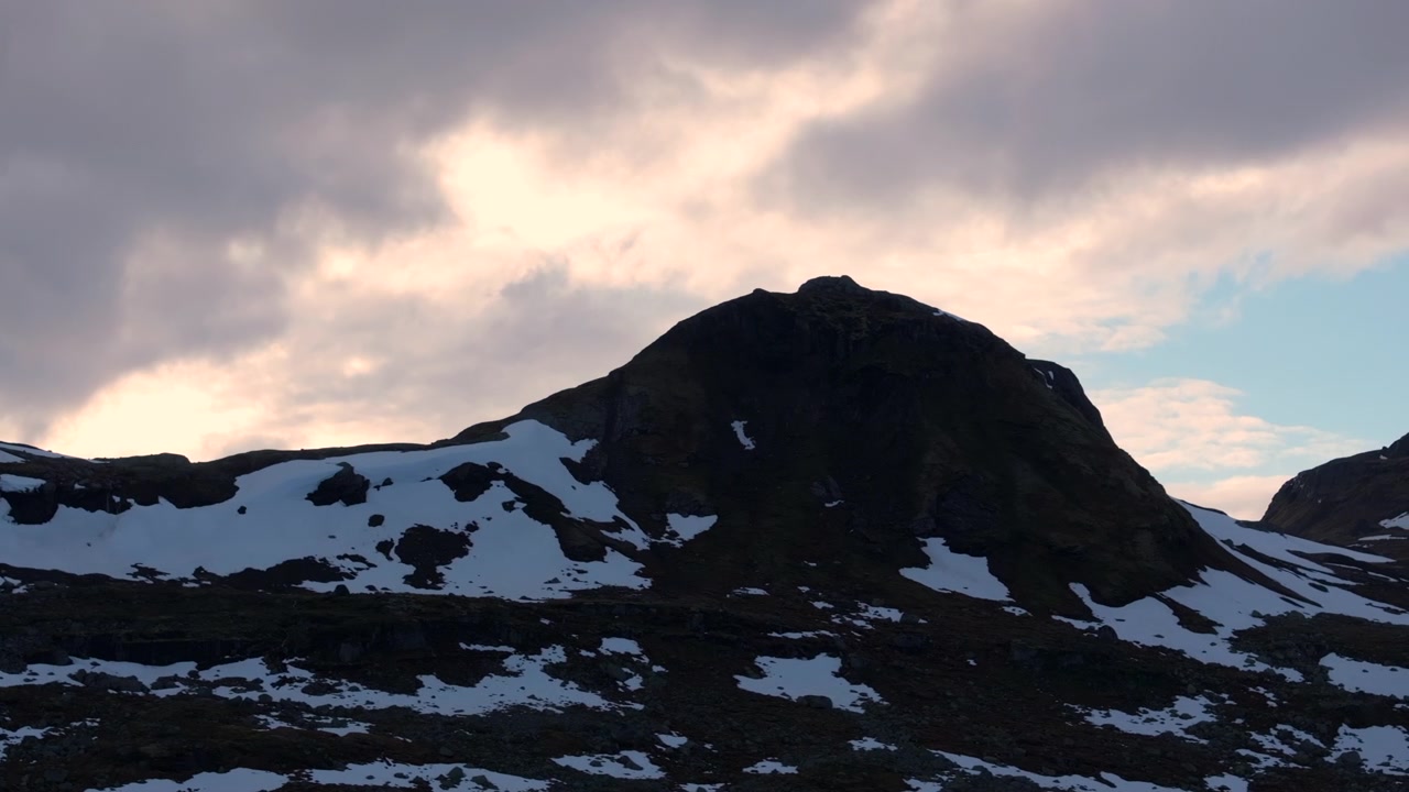 Kinematische Drohnenaufnahme, die während der goldenen Stunde entlang eines zerklüfteten Berggrats in einer abgelegenen Alpenlandschaft gleitet.