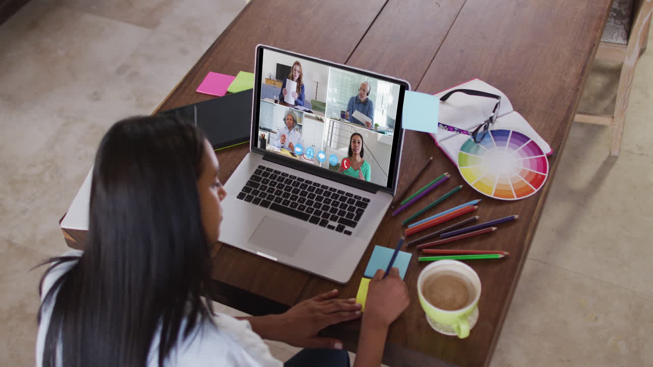mujer caucásica usando una computadora portátil en videollamada con colegas y tomando notas