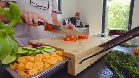 panning reveal shot of a person cutting a tomato on a wood cutting board inside a modern style kitchen with cut vegetables in preparation for a meal