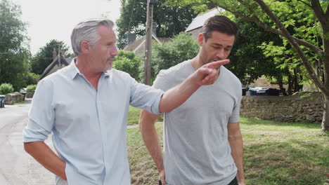 senior father with adult son talking as they walk along country road together