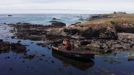 Toma-Panorámica-Aérea-De-Un-Barco-Pesquero-Naufragado-En-La-Playa-De-Cayucos-Cerca-De-Morro-Bay,-California