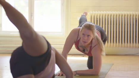 blonde yoga instructor demonstrates leg lift pose to class on mat in yoga studio