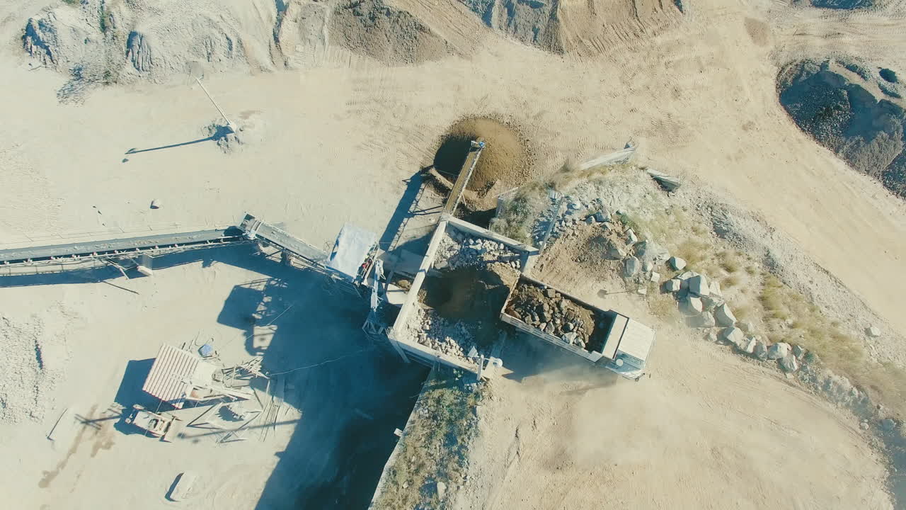 loaded truck driving into dusty crushed stone quarry gravel pit, wide aerial establishment shot