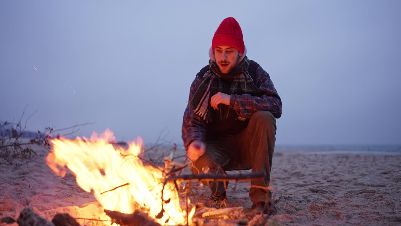 Man sitting by a campfire on the beach at sunset