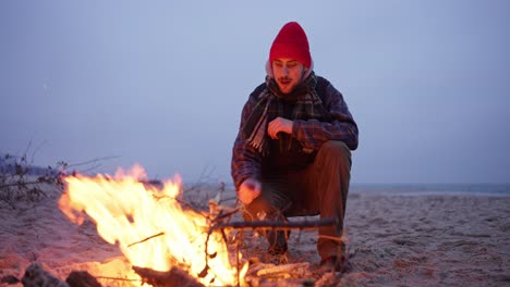 man sitting by a campfire on the beach at sunset