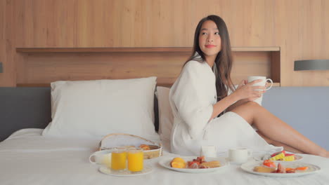 young woman in bathrobe enjoying breakfast in bed