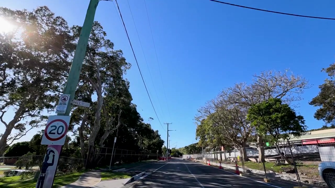 Perspectiva em primeira pessoa dirigindo por uma estrada de asfalto ensolarada ladeada por árvores em Crescent Head, Austrália