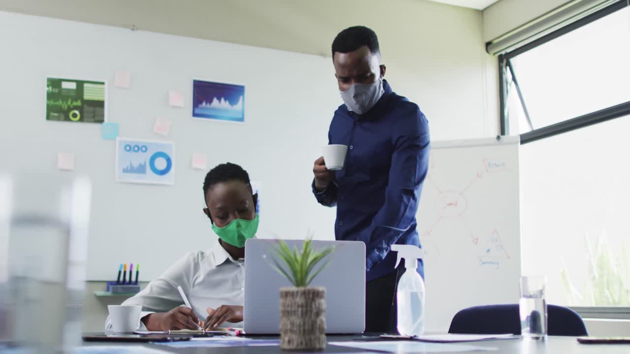 hombre afroamericano y mujer afroamericana con máscaras faciales discutiendo sobre computadora portátil en una reunión