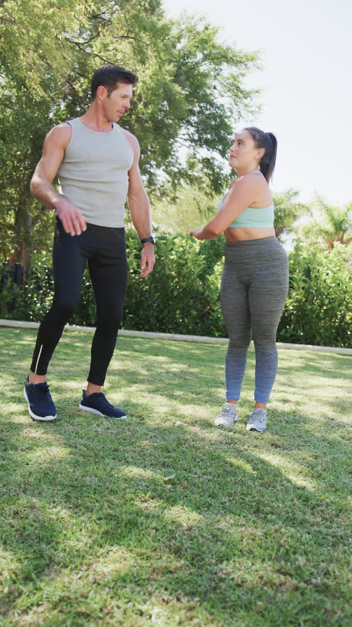 Vertical video of caucasian couple doing yoga and high fiving in garden, in slow motion
