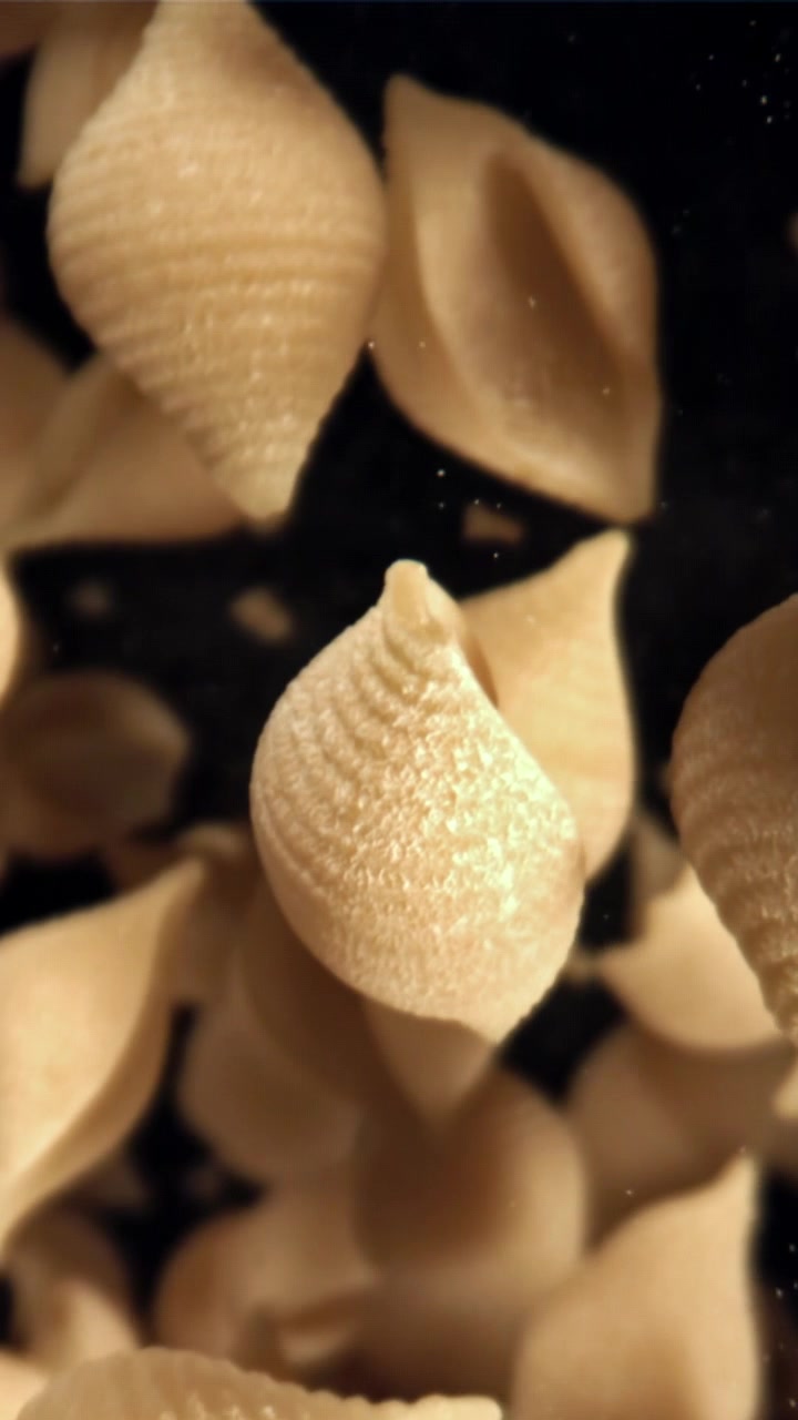 Pasta conchiglie secca che cade al rallentatore su sfondo scuro