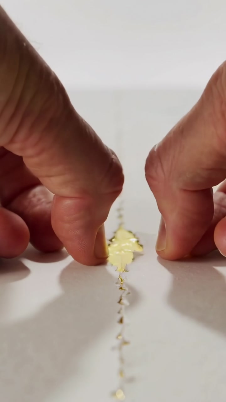 Vertical video: Scraping knife causing hands pulling dashed paper on table, revealing gold foil