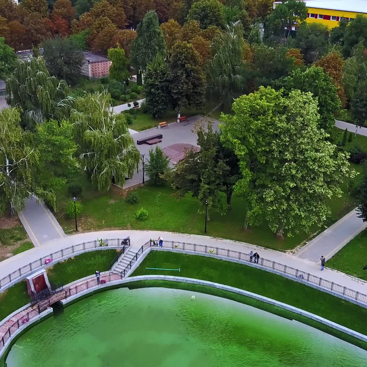 Wind blowing hard and shaking trees in the city park. Big fountain in the city garden. Aerial view