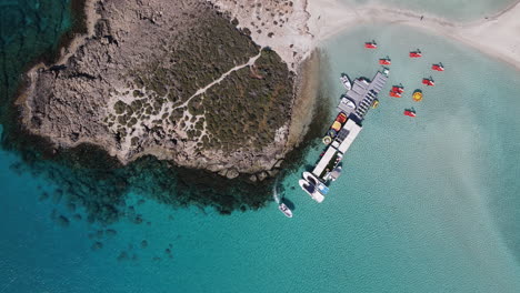 Nissi-beach-top-view-of-clear-waters,-rocky-shore,-boat-sailing-off-charming-small-dock,-Ayia-Napa-Cyprus