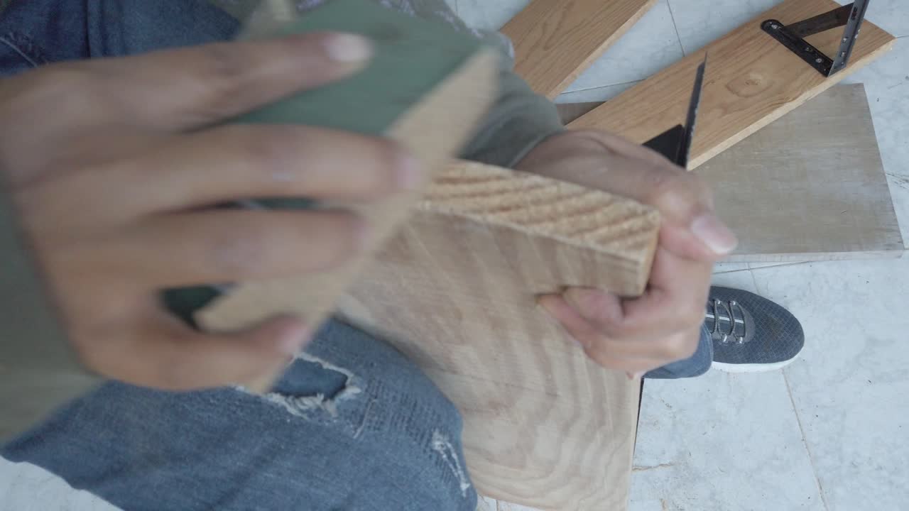 Primo piano di mani che levigano una tavola di legno con carta vetrata durante un lavoro di falegnameria di miglioramento della casa. Luce naturale, scena di laboratorio al chiuso