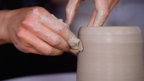 potter uses sponge to shape clay pot on her pottery wheel