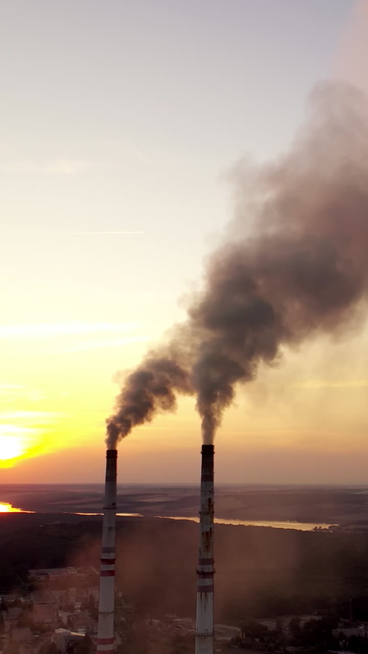 Environment pollution. Dark smoke going from two industrial pipes on nature background at sunset. Vertical video