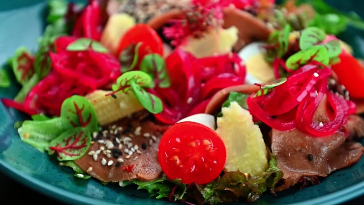 Insalata colorata con verdure e carne servita su un piatto blu. L’insalata è preparata con verdure fresche, carne e guarnizioni su un piatto blu.