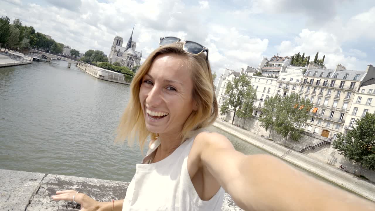 Jovem mulher tirando uma selfie em Paris, na Catedral de Notre Dame, usando um celular.