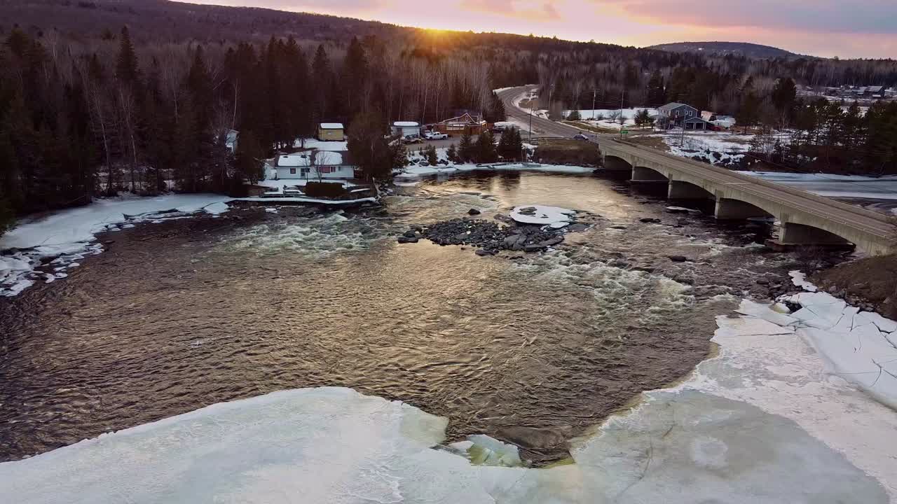 Ilmakuva joesta ja kylästä auringonlaskun aikaan talvella.