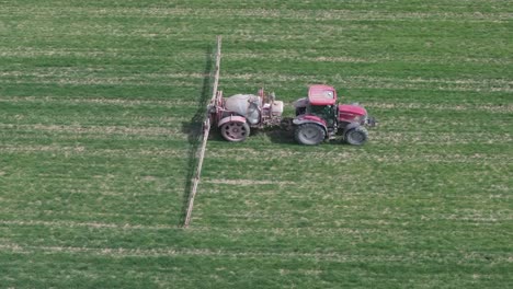 vuelo lateral con un dron filmando el trabajo agrícola llevado a cabo por un agricultor con su tractor rojo y su remolque de pulverización con grandes brazos extensibles en un campo cultivado con plantas verdes toledo