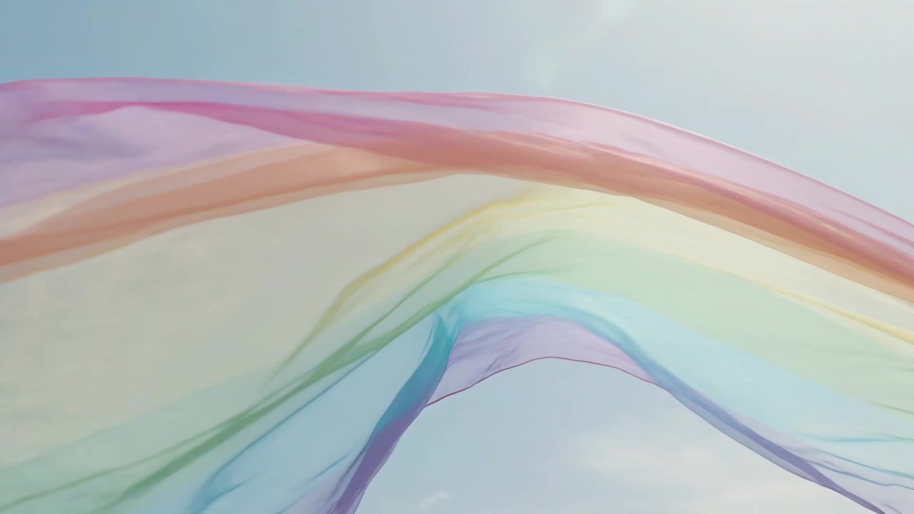 Drifting in light breeze sheer rainbow ribbon flowing across blue sky, showing folds and sun glare