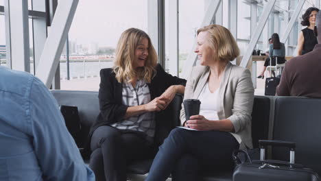 two businesswomen sitting in airport departure talking together