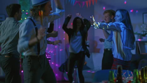 at the college house costume party: diverse group of friends have fun, dancing and socializing and drinking. stylish boys and girls dance in the living room. disco neon lights illuminating room. slow motion.