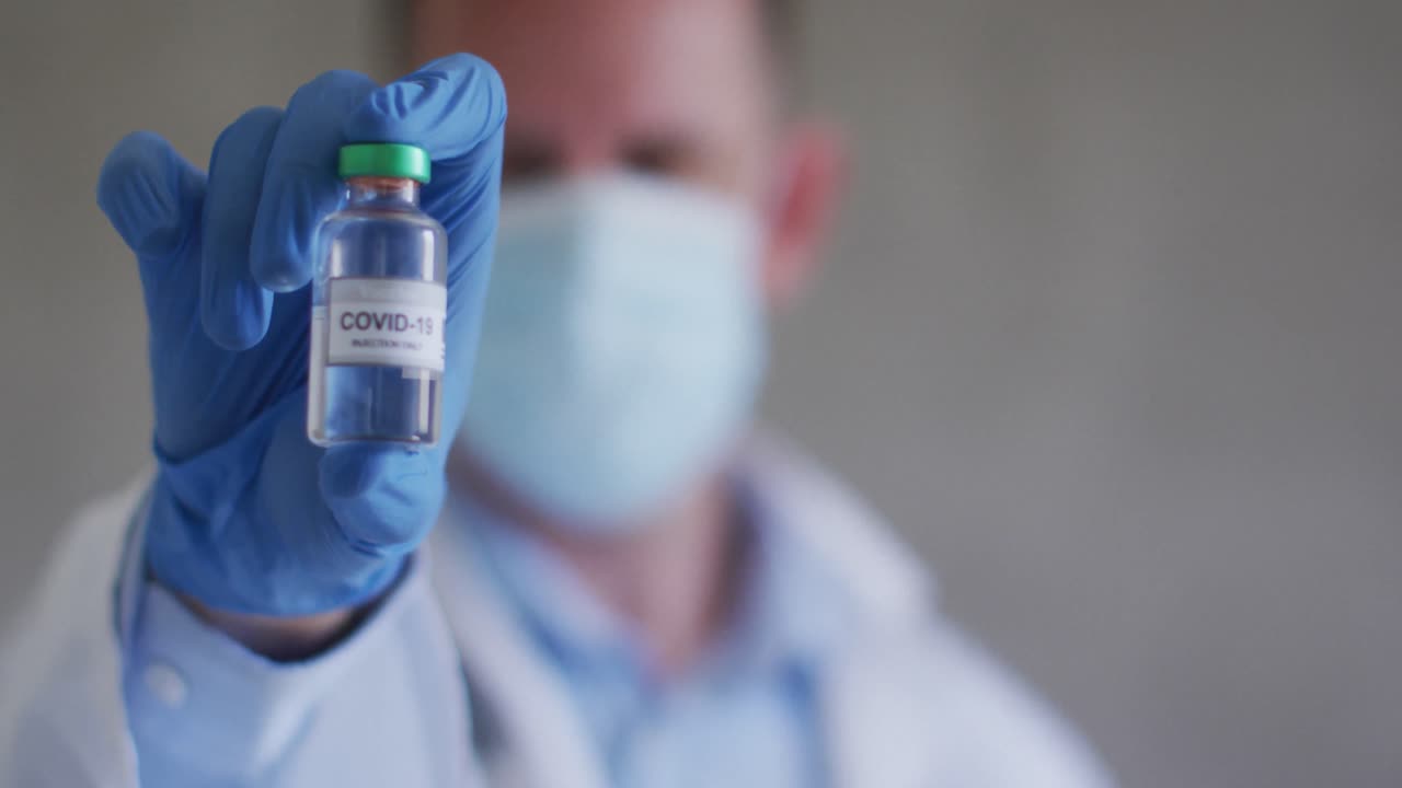 médico caucásico con máscara facial y vacuna en la mano