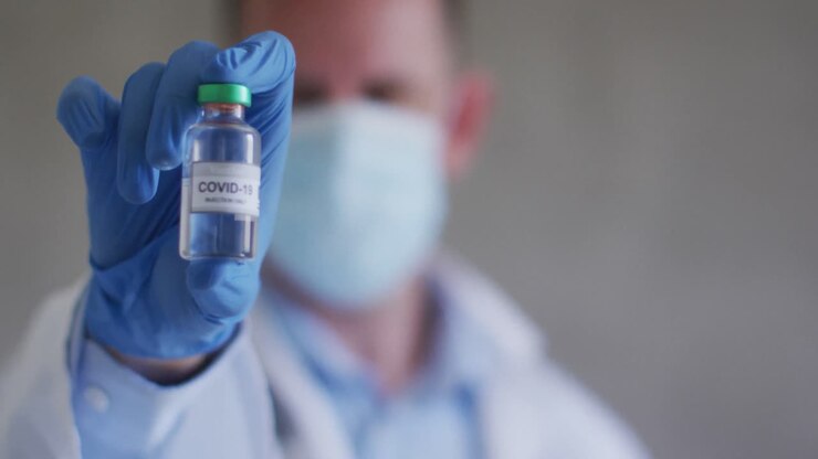 Caucasian male doctor wearing face mask and holding vaccine