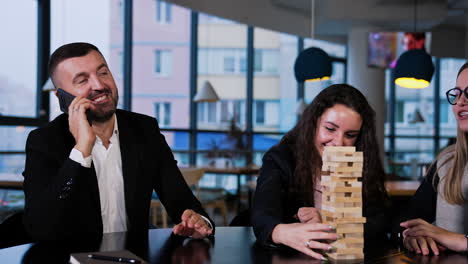 company of office people plating jenga and having fun. one of the male players distracted to talk on the phone.