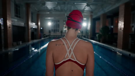 a female swimmer stands at the edge of a swimming pool ready to start a race