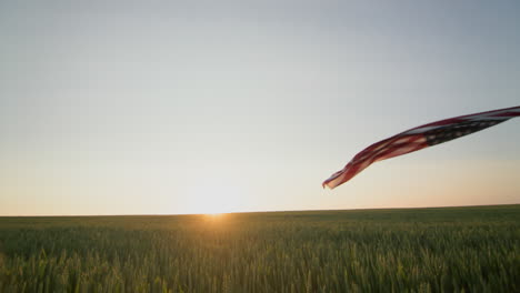 american farmer waving the us flag against the backdrop of a field of wheat where the sun rises. pov view