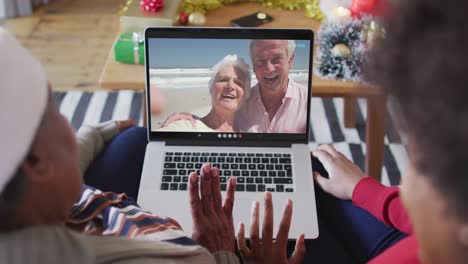 African-american-mother-and-daughter-using-laptop-for-christmas-video-call-with-couple-on-screen