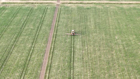 aerial drone tracking shot following a tractor with long boom sprayer as it moves along regular rows inside a maize field, applying crop treatment and illustrating modern agricultural practices