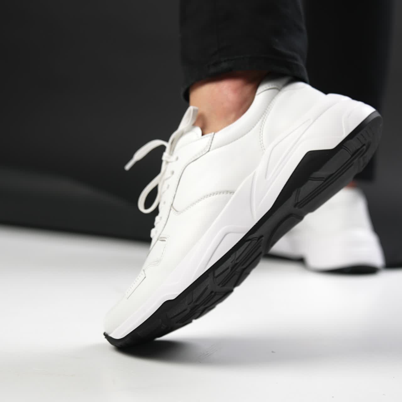 White modern stylish sneakers demonstration. Male putting his foot in fashionable shoes in front of camera on the floor. Close up. Blurred backdrop