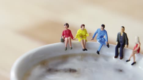 miniature business people sitting on the edge of the coffee cup