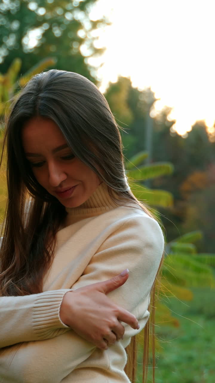 Resilient dark- haired young woman posing in front of camera. Lady smiling happily waving her long hair. Autumn park at backdrop.