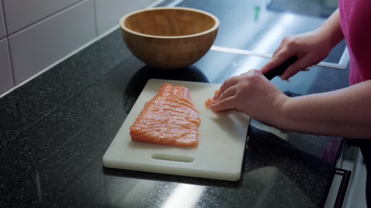 Static shot of woman hands cutting raw salmon in slices, interior