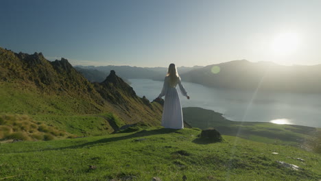 elegant woman in white dress standing on mountain slope with bright sunlight