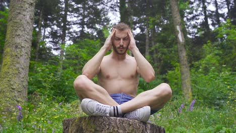 man rubbing his head in the forest.