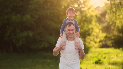 Un-Padre-Amoroso-Sonríe-Caminando-Con-El-Niño-Sentado-En-El-Cuello-Al-Atardecer-En-Un-Prado-En-Verano-En-Cámara-Lenta.