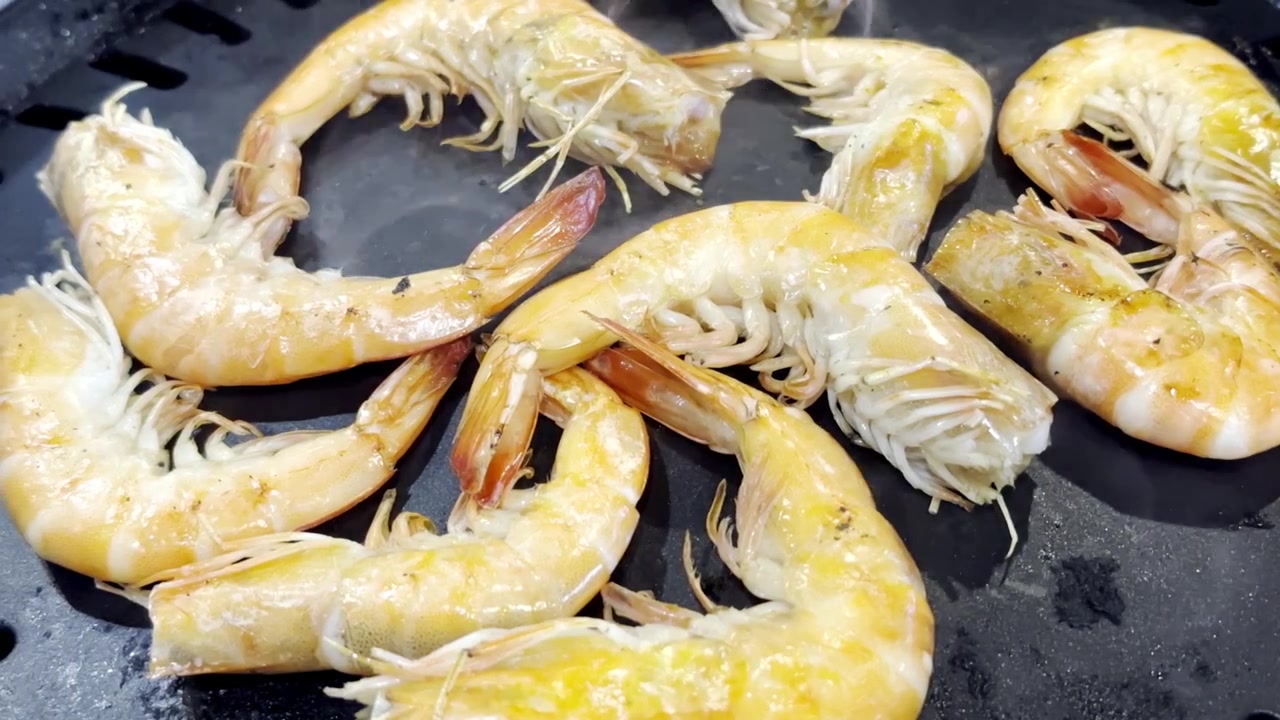 Primo piano di gamberi freschi che sfrigolano su una padella calda da barbecue, catturando frutti di mare succosi, vapore che sale e deliziosi sapori grigliati in una scena di cucina.
