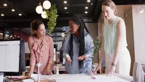 Diverse-female-architects-discussing-work-and-looking-at-blueprints-at-office,-in-slow-motion