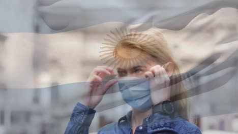 Animation-of-flag-of-argentina-waving-over-caucasian-woman-wearing-face-mask-in-city-street