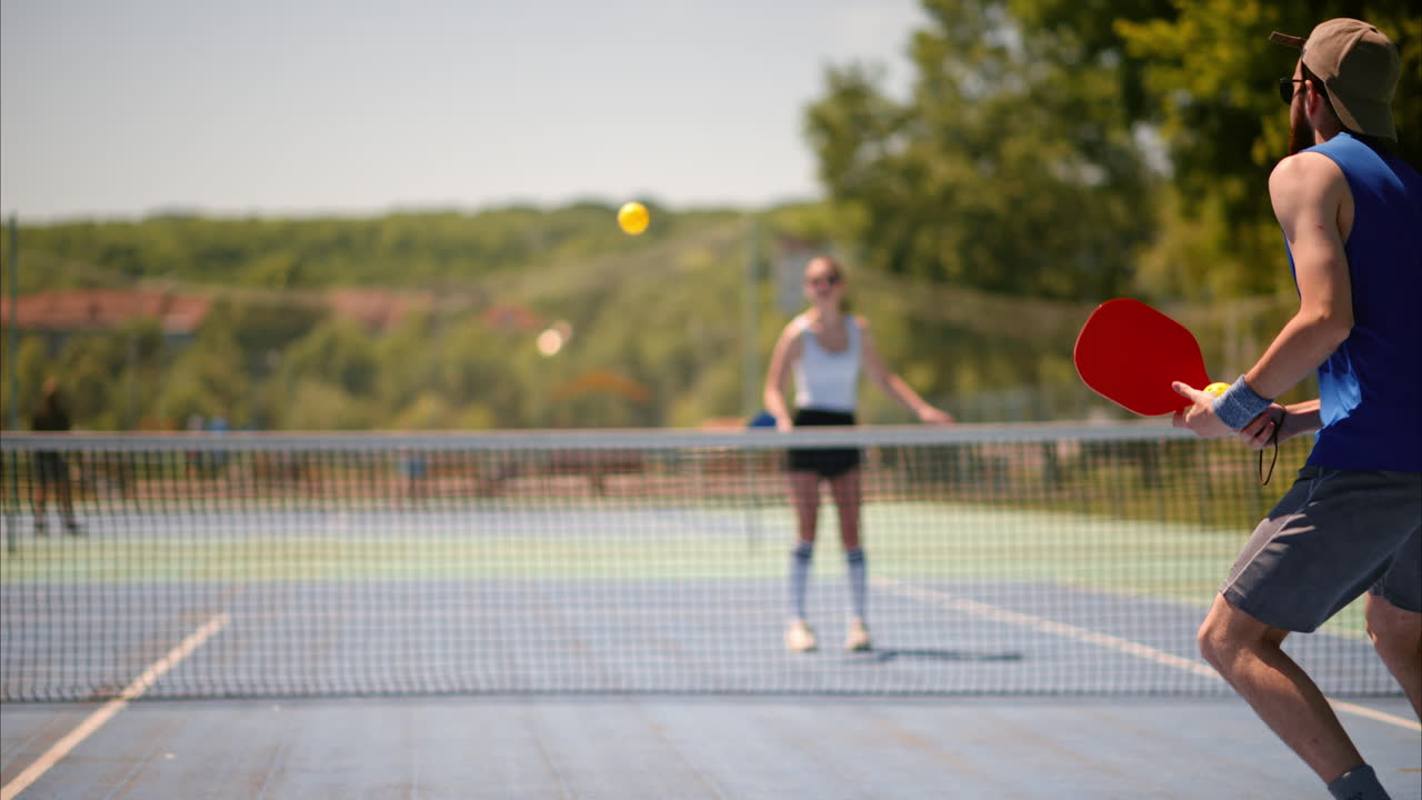 En mann og en kvinne som spiller pickleball på en solskinnsdag