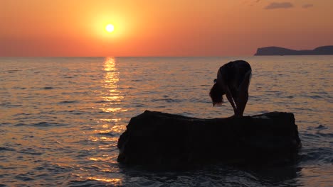 mujer joven plantea ejercicios de meditación de yoga sobre un gran acantilado bañado por el mar en la hermosa puesta de sol