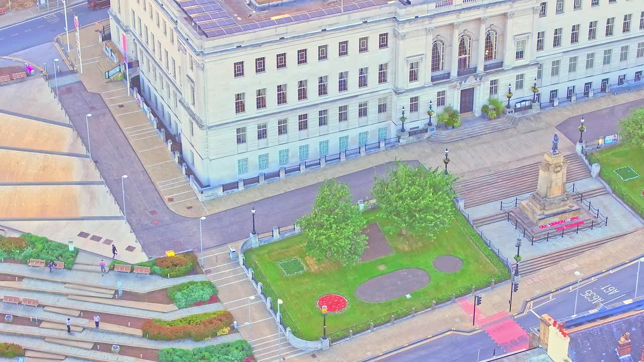 Drone view of Barnsley War Memorial in front of the neoclassical Town Hall, with red poppy wreaths, symmetrical formal garden layout, stepped plaza, and clean civic architecture at sunset